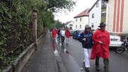 Pitschedabber mit Regenschutz laufen eine Straße entlang. Vorne Achim mit Alwin