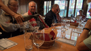 am Tisch: auf dem Tisch Gläser, Wein wird aus einer Flasche eingegossen, von links Marlene, Volkhard, Alwin, Achim 
