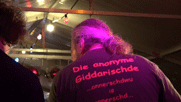 der Sänger Etzel von hinten mit Aufschrift auf seinem T-Shirt: Die anonyme Giddarischde und dem Zitat ... annerschdwu is annerschd...