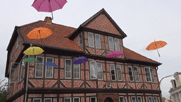 Backstein-Fachwerkhaus, davor zur Dekoration in der Einkaufsstraße aufgehängte bunte Schirme