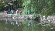 Pitschedabber laufen auf dem Weg zum "Küchengarten" entlang eines Teiches, in dem sich die Gruppe spiegelt.